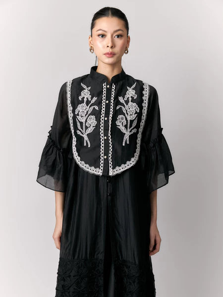 Woman wearing a black dress with white floral embroidery vest by Studio Tui on a plain background