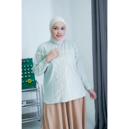 Woman wearing a light green shirt by Abame and beige skirt in an indoor setting