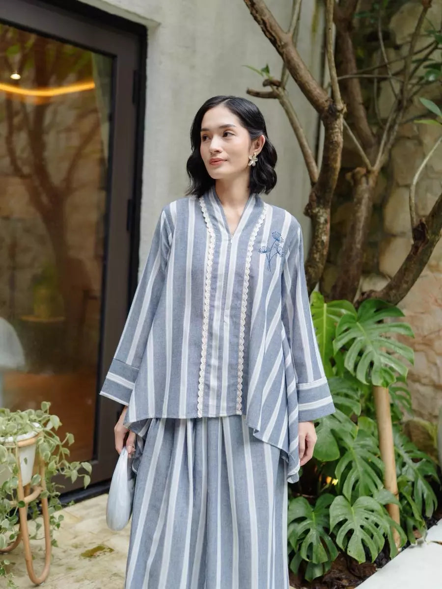 Woman wearing a denim color striped outfit set by Haidee Orlin standing outdoors with plants and a building in the background
