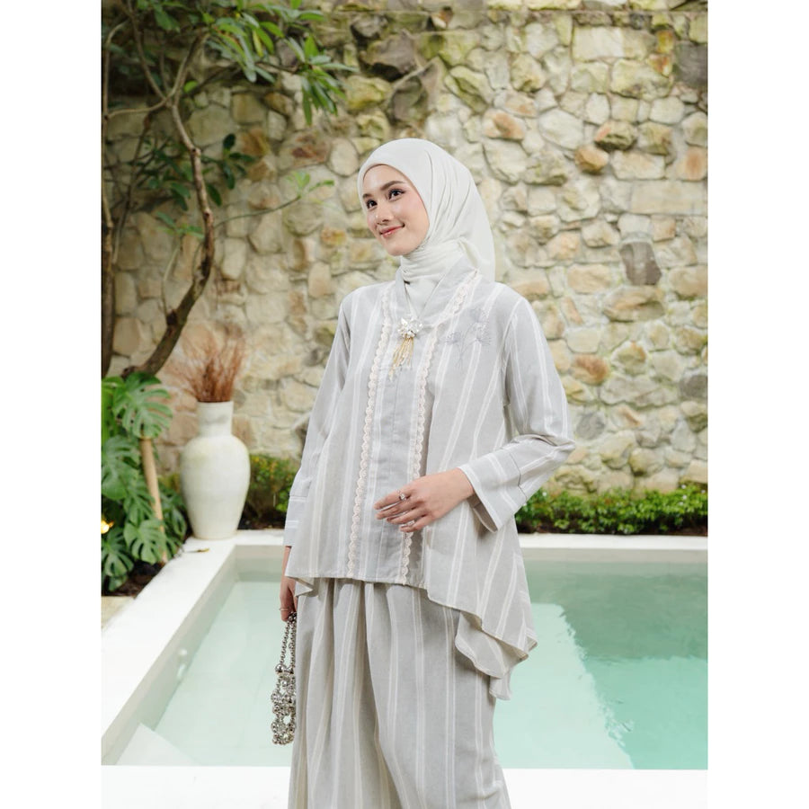 Woman in a silver outfit set by Haidee Orlin standing by a pool with a stone wall and plants in the background