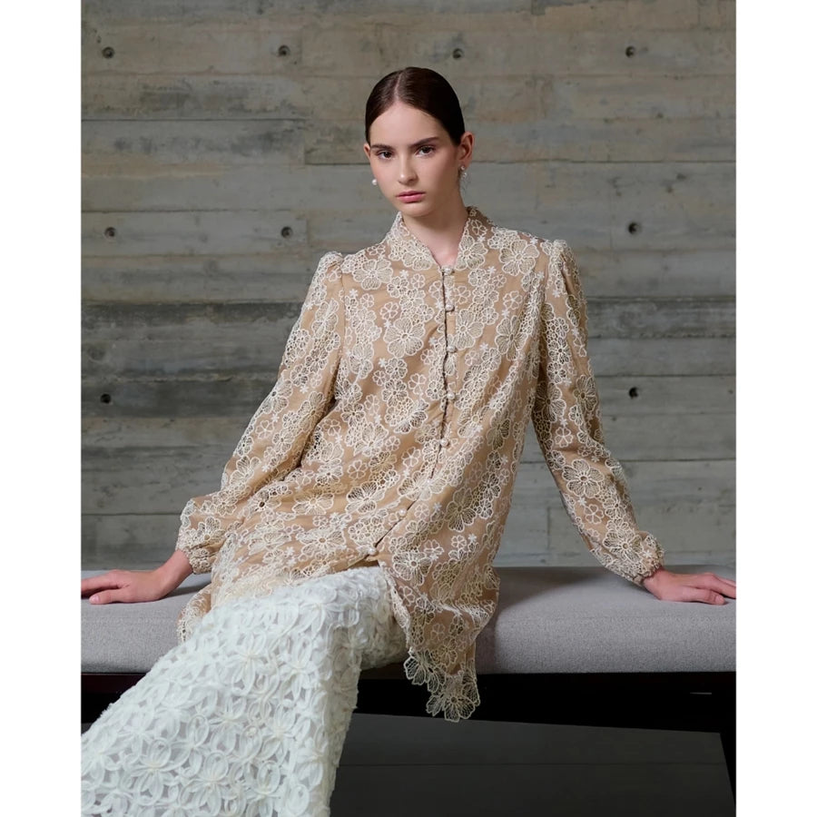 Woman wearing a beige lace long blouse by Kasa Heritage sitting on a bench against a wooden wall.