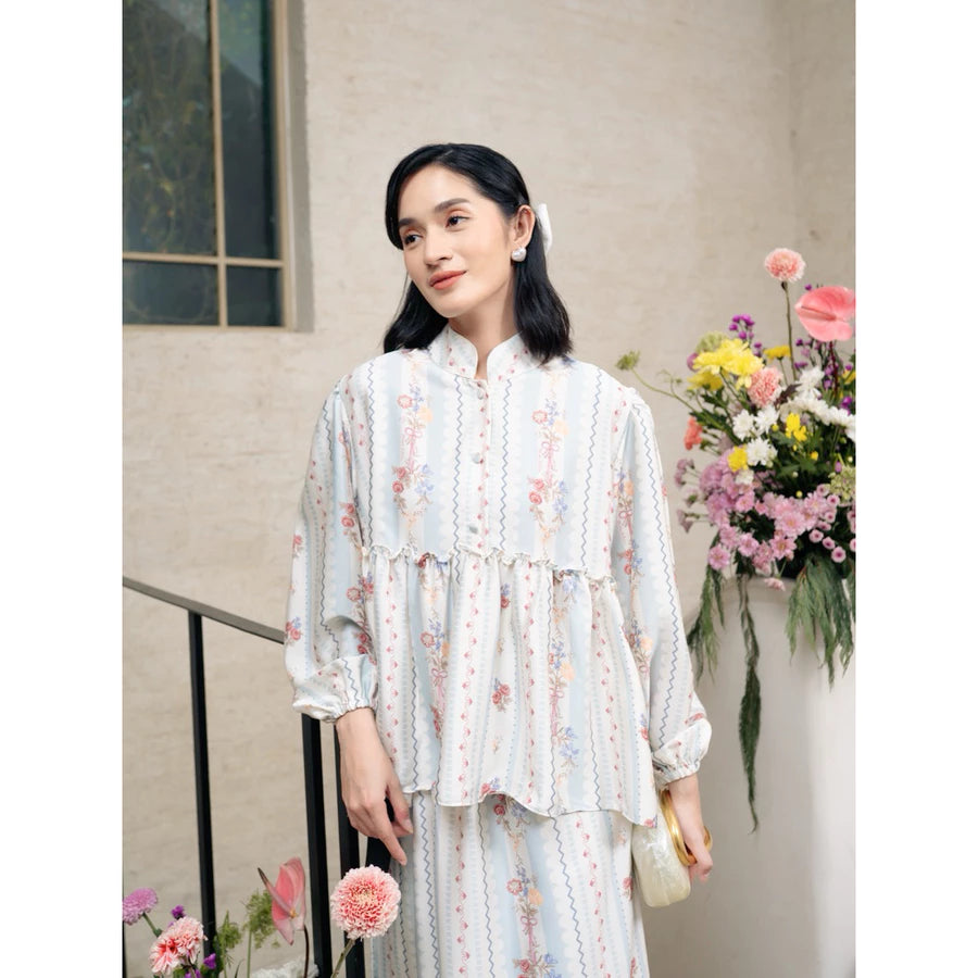 Woman in a floral outfit set by Haidee Orlin with blue accents standing outdoors with flowers in the background