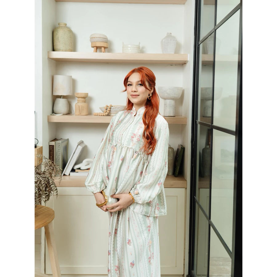 Woman in a floral outfit set by Haidee Orlin with sage accents standing in a room with shelves and decor.