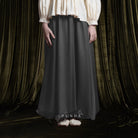Person wearing a long dark grey baloon sheer skirt by BWBYAZ with a white blouse against a draped curtain background.