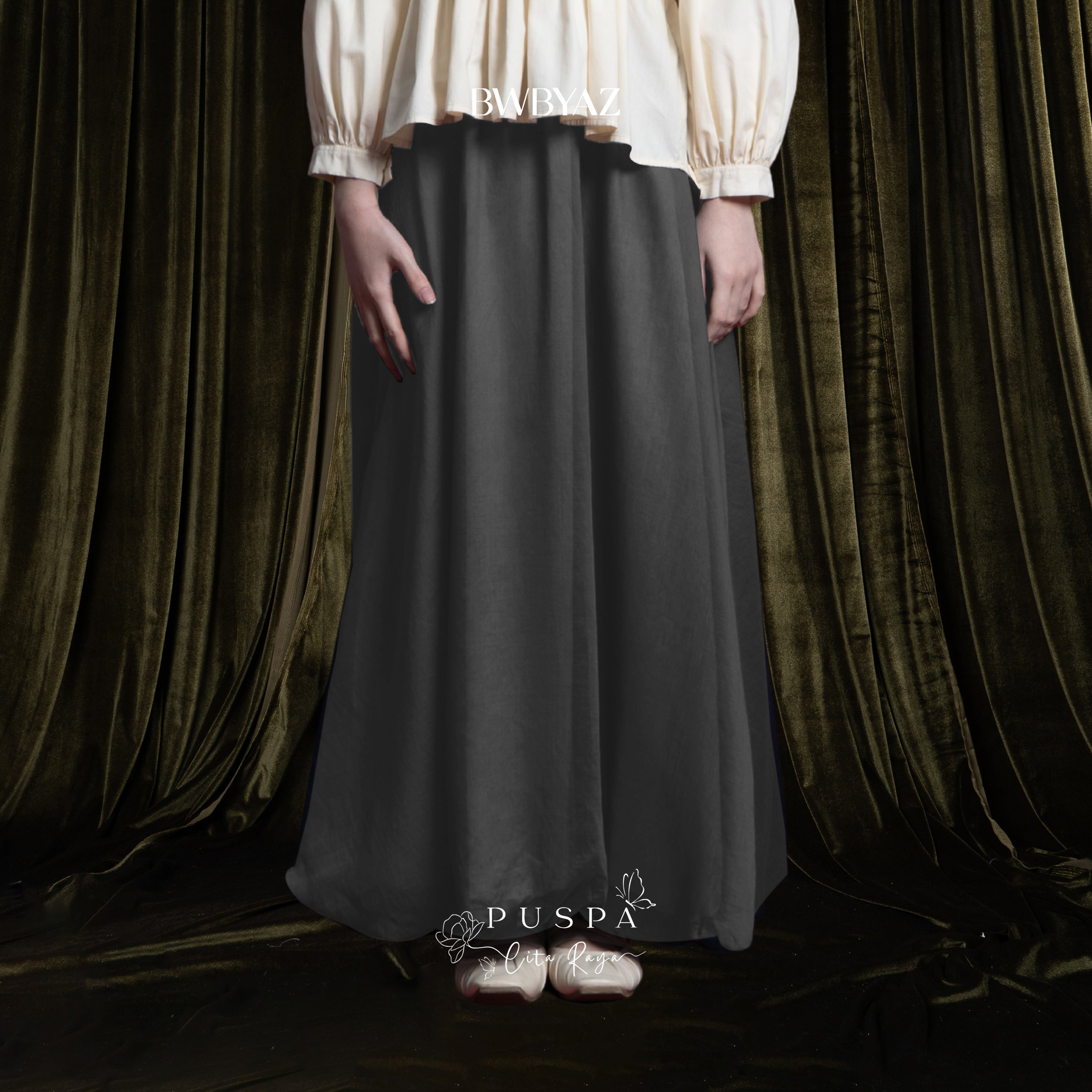 Person wearing a long dark grey baloon sheer skirt by BWBYAZ with a white blouse against a draped curtain background.