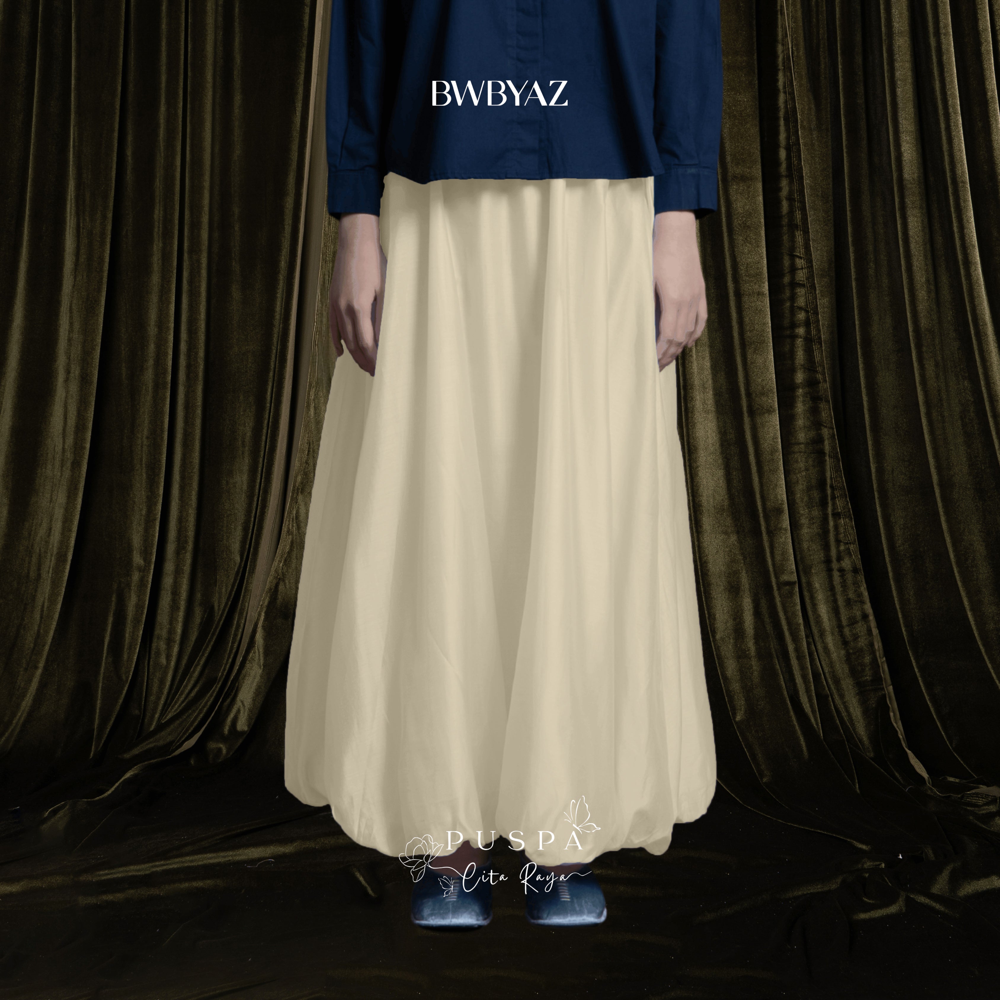 Person wearing a blue shirt and a beige baloon sheer skirt by BWBYAZ against a dark curtain background.