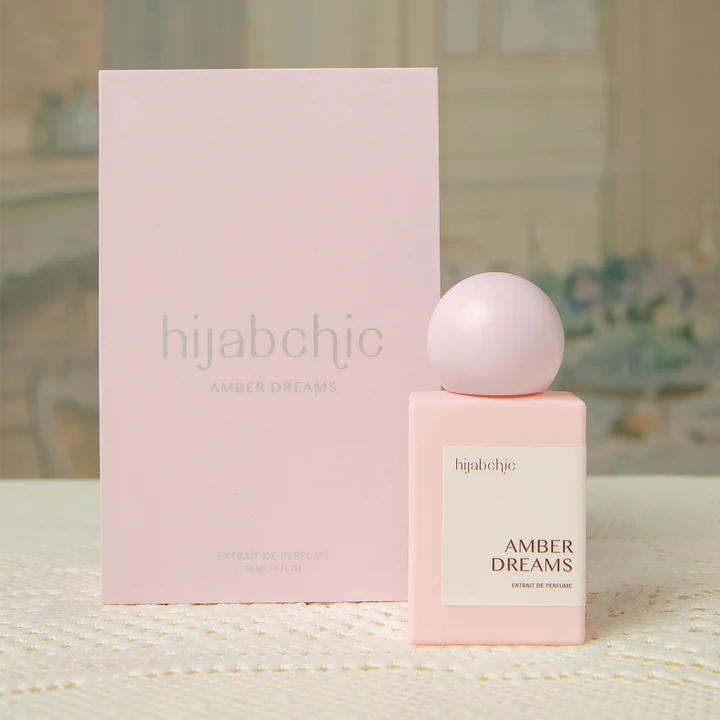 Pink hijabchic Amber Dreams perfume bottle and packaging on a textured surface with blurred background