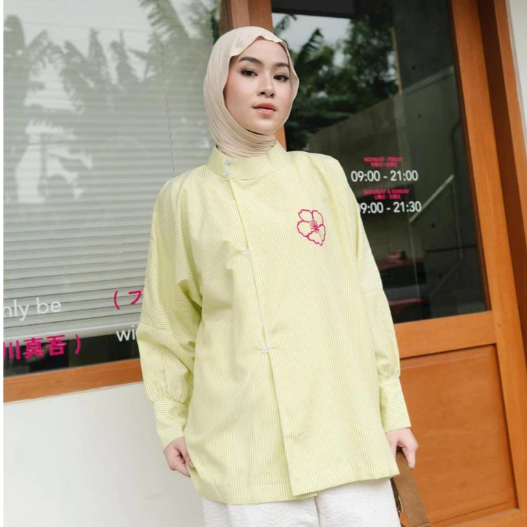 Woman wearing a lime color blouse by Haidee Orlin with a pink flower design in front of a glass door.