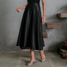 Person wearing a black satin skirt by Holy Peony in an urban setting with concrete walls and wooden steps.