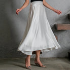 Person wearing a white satin skirt by Holy Peony with a gray concrete wall background