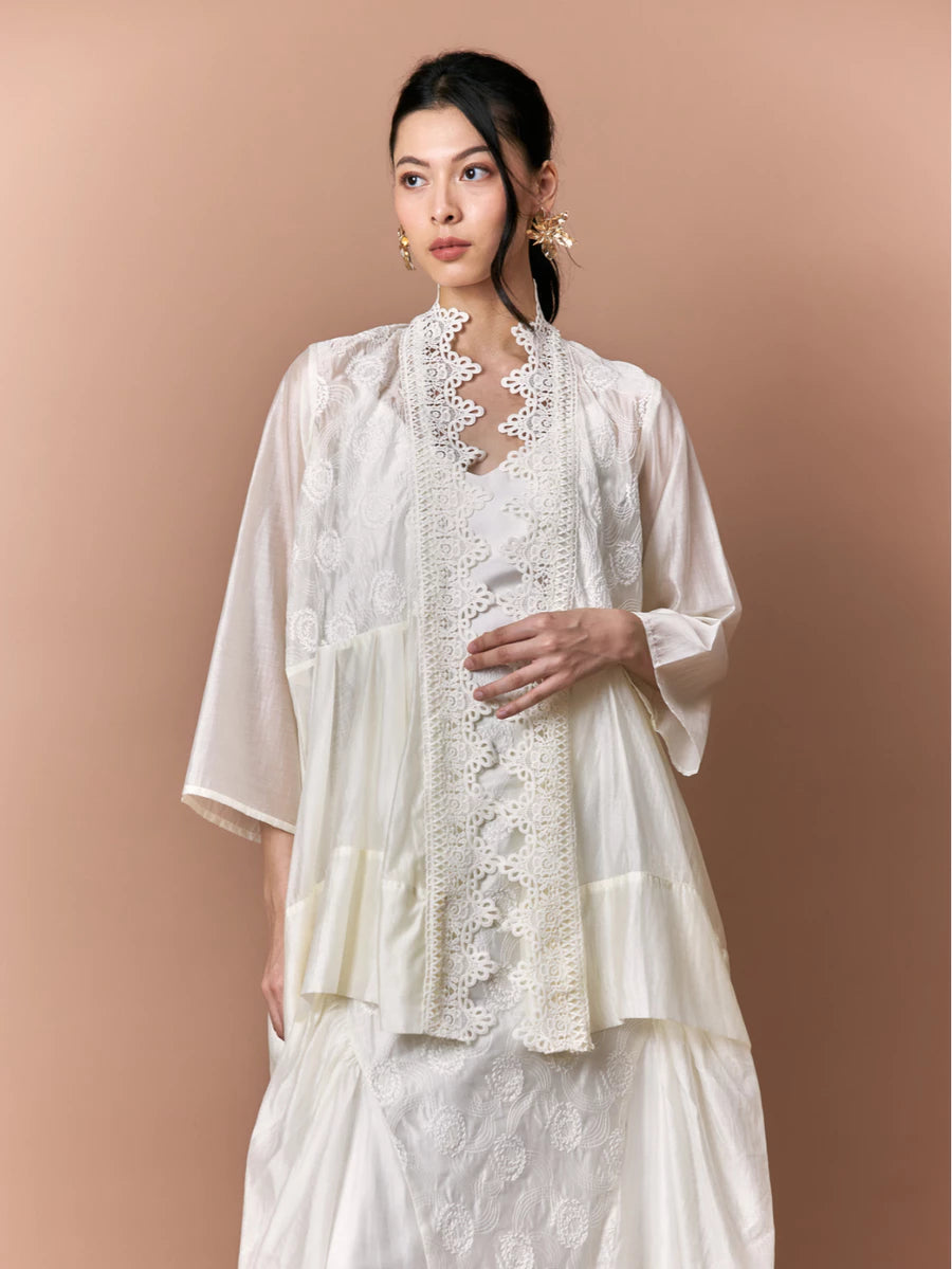 Woman wearing a white lace outer by Studio Tui against a beige background