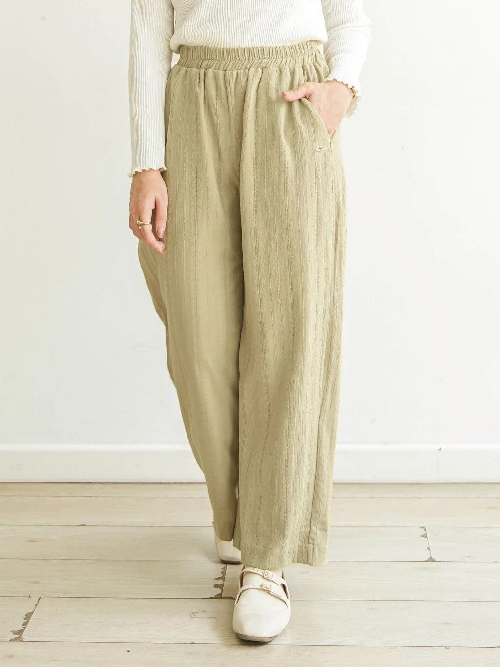 Person wearing light green wide-leg pants by Mistyvori and a white top on a light wooden floor with a white wall background.