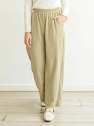 Person wearing light green wide-leg pants by Mistyvori and a white top on a light wooden floor with a white wall background.