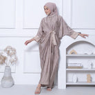 Woman in a light brown dress by Kartinis Label with a matching hijab standing in a minimalistic room.