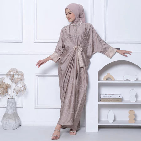 Woman in a light brown dress by Kartinis Label with a matching hijab standing in a minimalistic room.