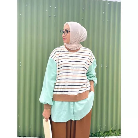 Woman wearing a striped shirt by Abame and hijab standing against a green corrugated metal background