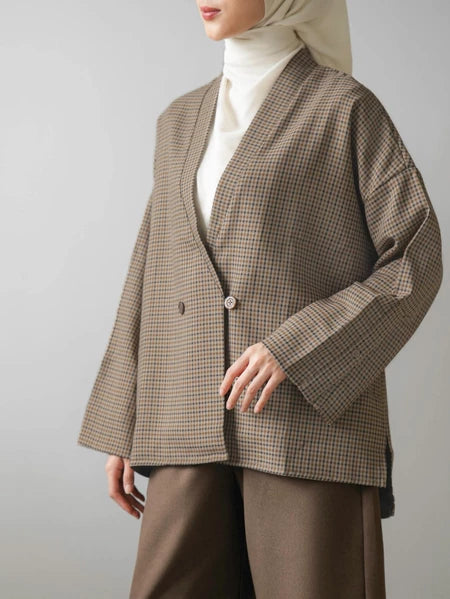 Person wearing a brown checkered blazer by Mistyvori over a white shirt with a beige hijab on a gray background