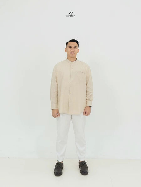A man standing against a white background, wearing a beige long-sleeved shirt by Swifter with a classic design.