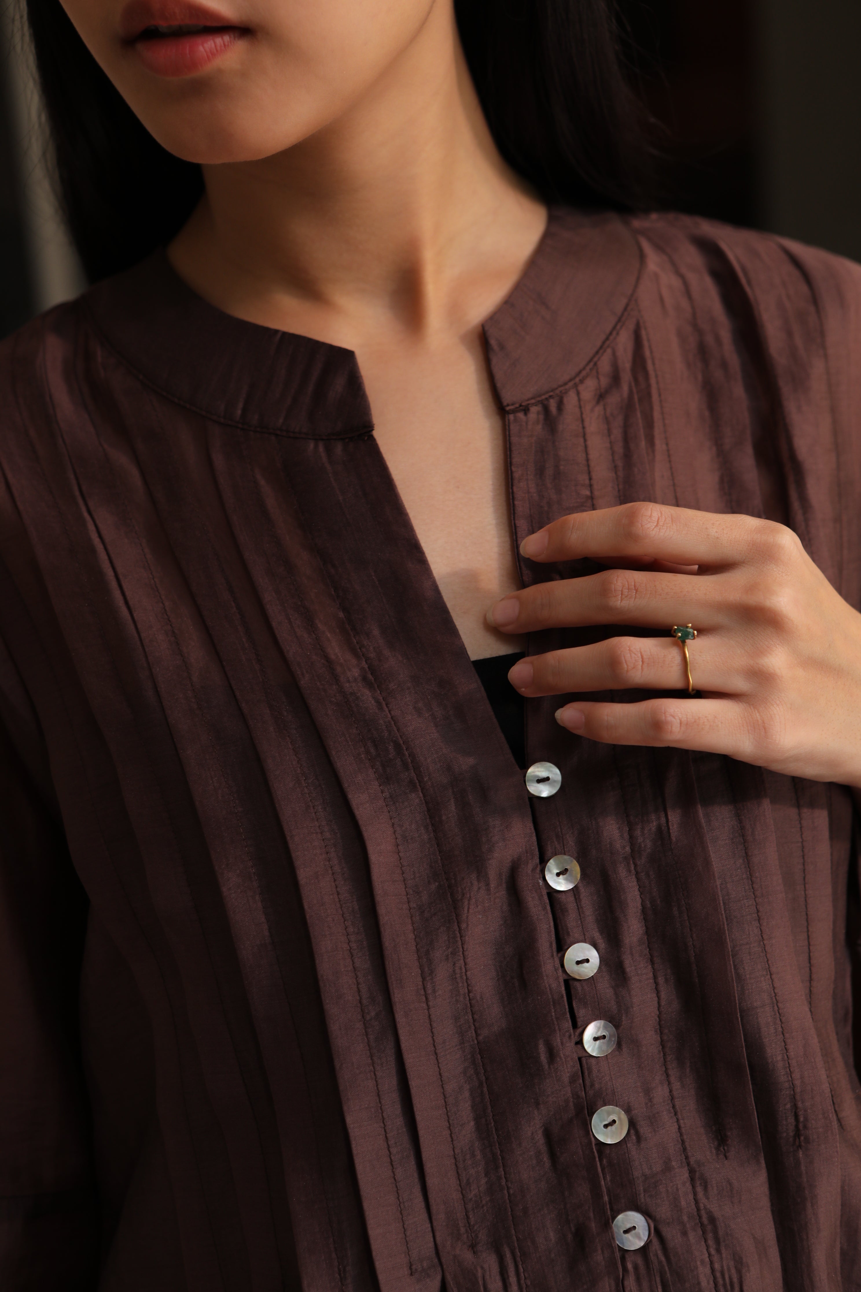 Close-up of a person wearing a dark brown blouse by Kasyalia with buttons and a ring on a dark background