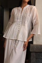 White blouse by Kasyalia with sheer overlay held by a person on a neutral background