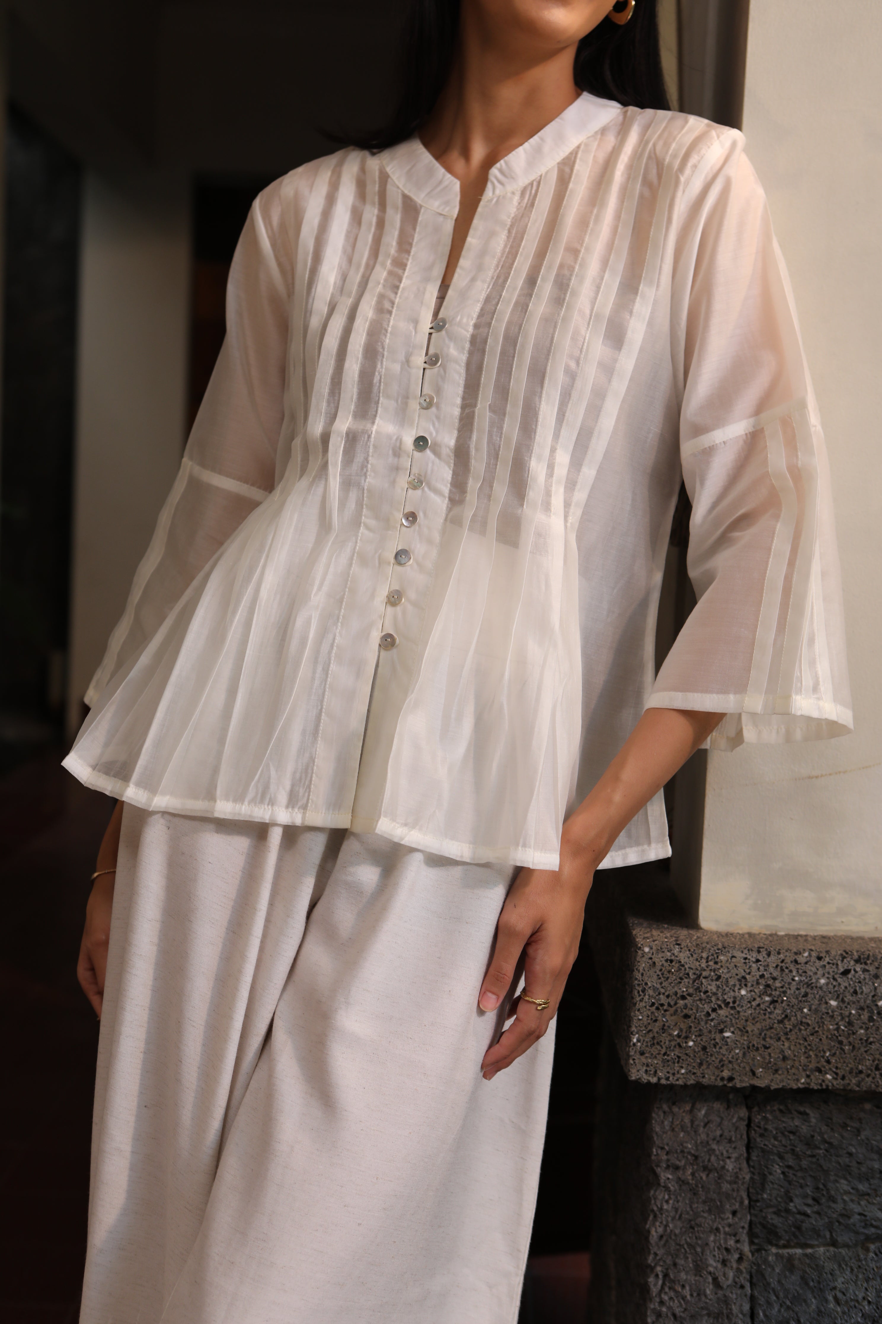 White blouse by Kasyalia with sheer overlay held by a person on a neutral background