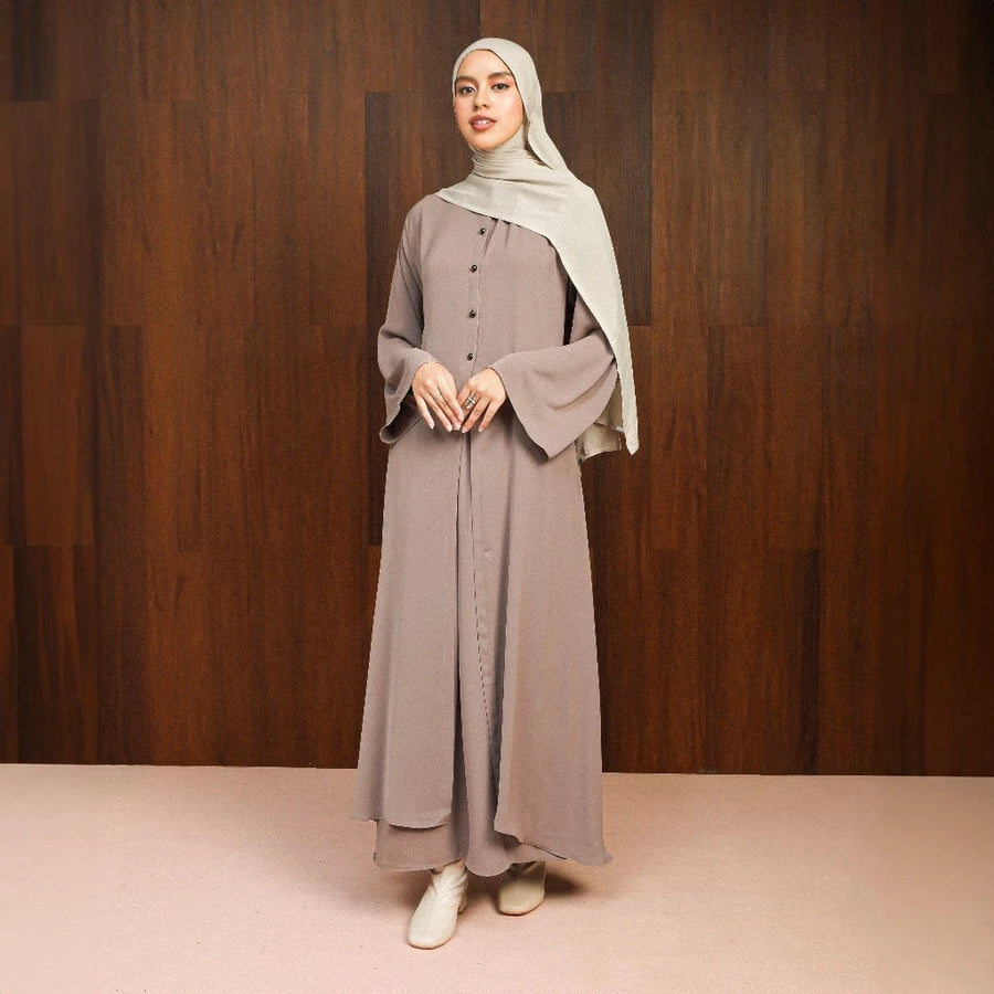 Woman wearing a long, light brown abaya dress by Lozy Hijab with a hijab against a wooden background