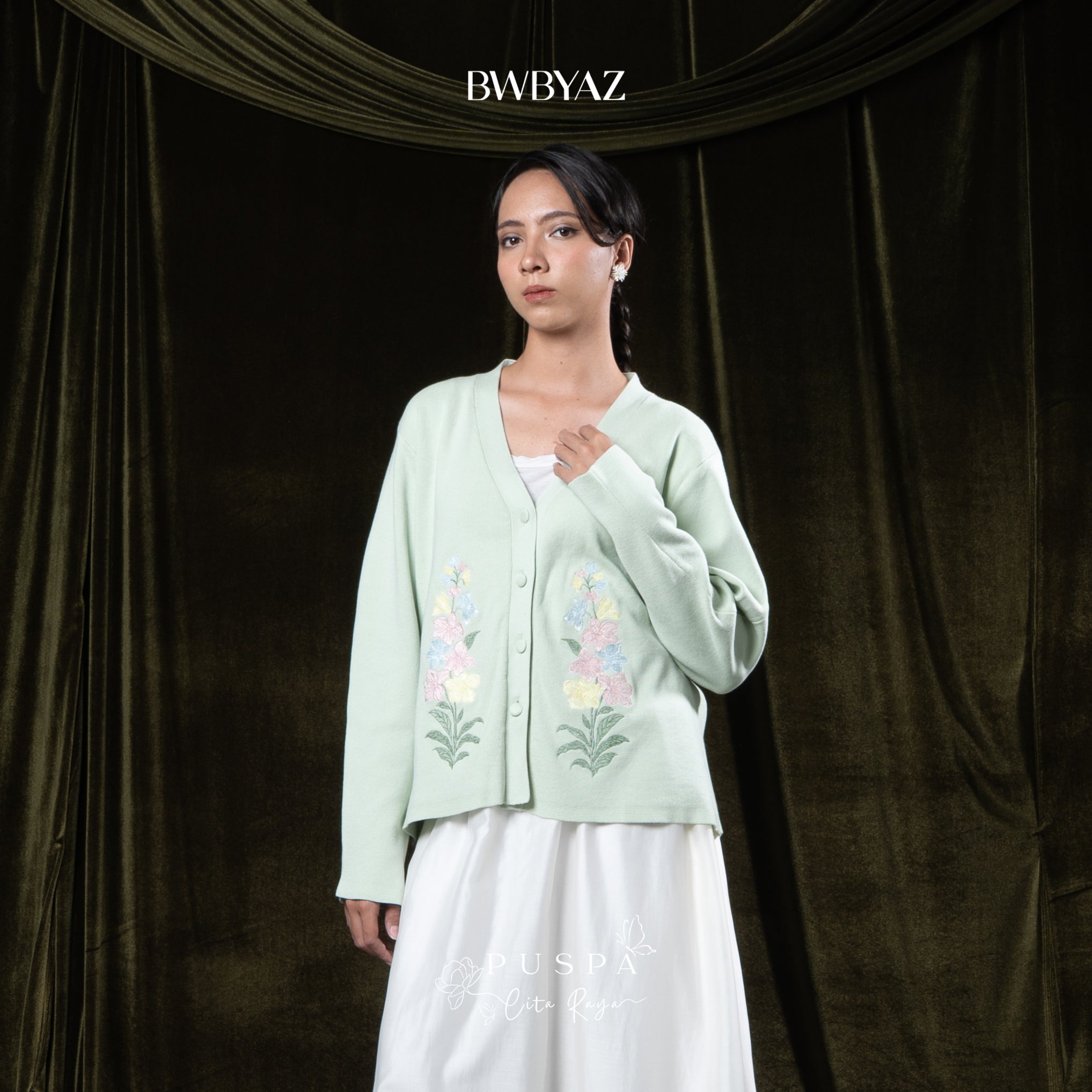 Woman wearing a light green embroidered cardigan over a white outfit against a dark curtain background with 'BWBYAZ' branding.