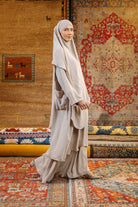 A woman wearing a beige Lozy Hijab abaya set, which includes a long dress and a matching headscarf.
