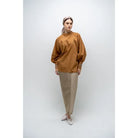 A person wearing a brown, long-sleeved blouse by Glashka with a round neckline and decorative buttons on the cuffs. The blouse has a loose fit and the person is paired with black pants.