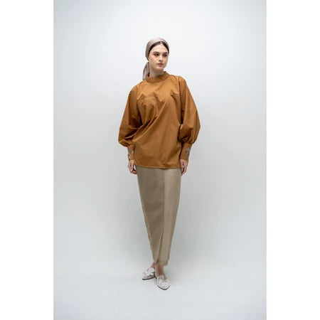 A person wearing a brown, long-sleeved blouse by Glashka with a round neckline and decorative buttons on the cuffs. The blouse has a loose fit and the person is paired with black pants.