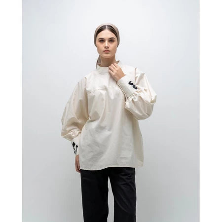 A person wearing a white, long-sleeved blouse by Glashka with a round neckline and decorative buttons on the cuffs. The blouse has a loose fit and the person is paired with black pants.