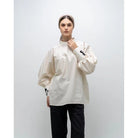 A person wearing a white, long-sleeved blouse by Glashka with a round neckline and decorative buttons on the cuffs. The blouse has a loose fit and the person is paired with black pants.