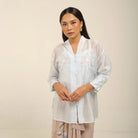 Woman wearing a light blue kebaya by Kartinis Label with floral patterns on a beige background