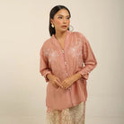 Woman wearing a pink embroidered kebaya by Kartinis Label with a plain background