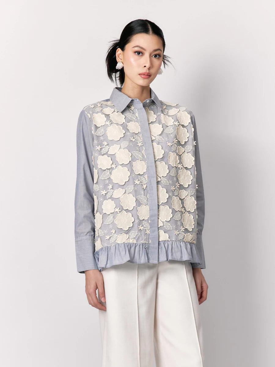 Woman wearing a light blue shirt by Studio Tui with floral lace overlay on a plain background