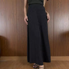 Person wearing black textured skirt by Renaette against a wooden panel background