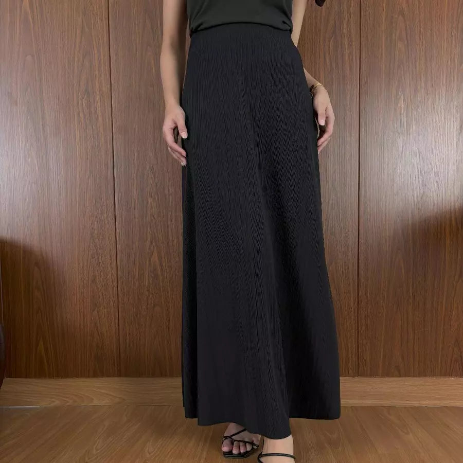 Person wearing black textured skirt by Renaette against a wooden panel background