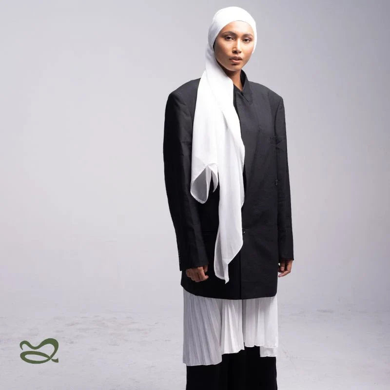 A woman wearing a white pashmina headscarf over a black outfit against a grey background.