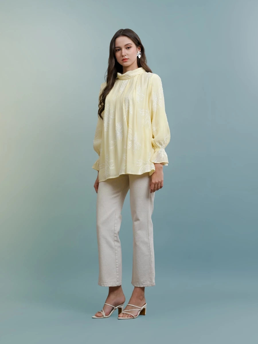 Woman wearing a light yellow blouse and white pants by Kasa Heritage against a gradient background