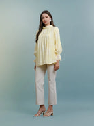 Woman wearing a light yellow blouse and white pants by Kasa Heritage against a gradient background
