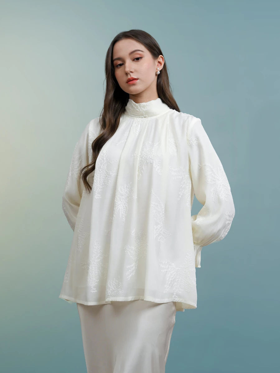 Woman wearing a white blouse with long sleeves by Kasa Heritage against a gradient blue background
