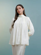 Woman wearing a white blouse with long sleeves by Kasa Heritage against a gradient blue background
