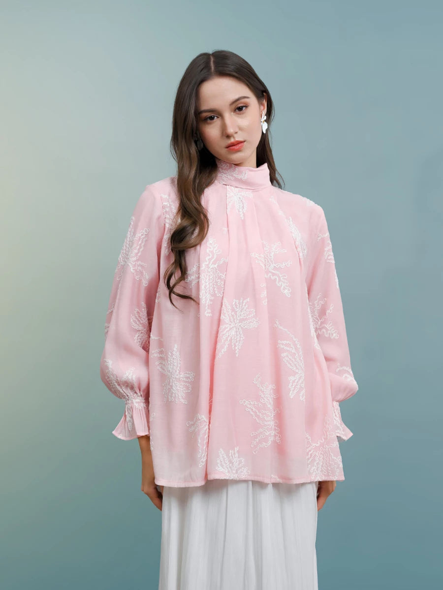 Woman wearing a pink blouse with white floral patterns by Kasa Heritage on a gradient background