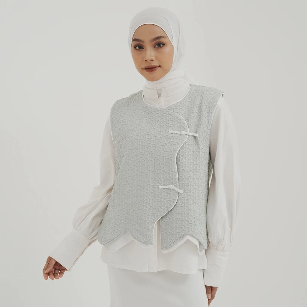 Woman wearing a light gray textured vest by Tunique over a white shirt on a plain background