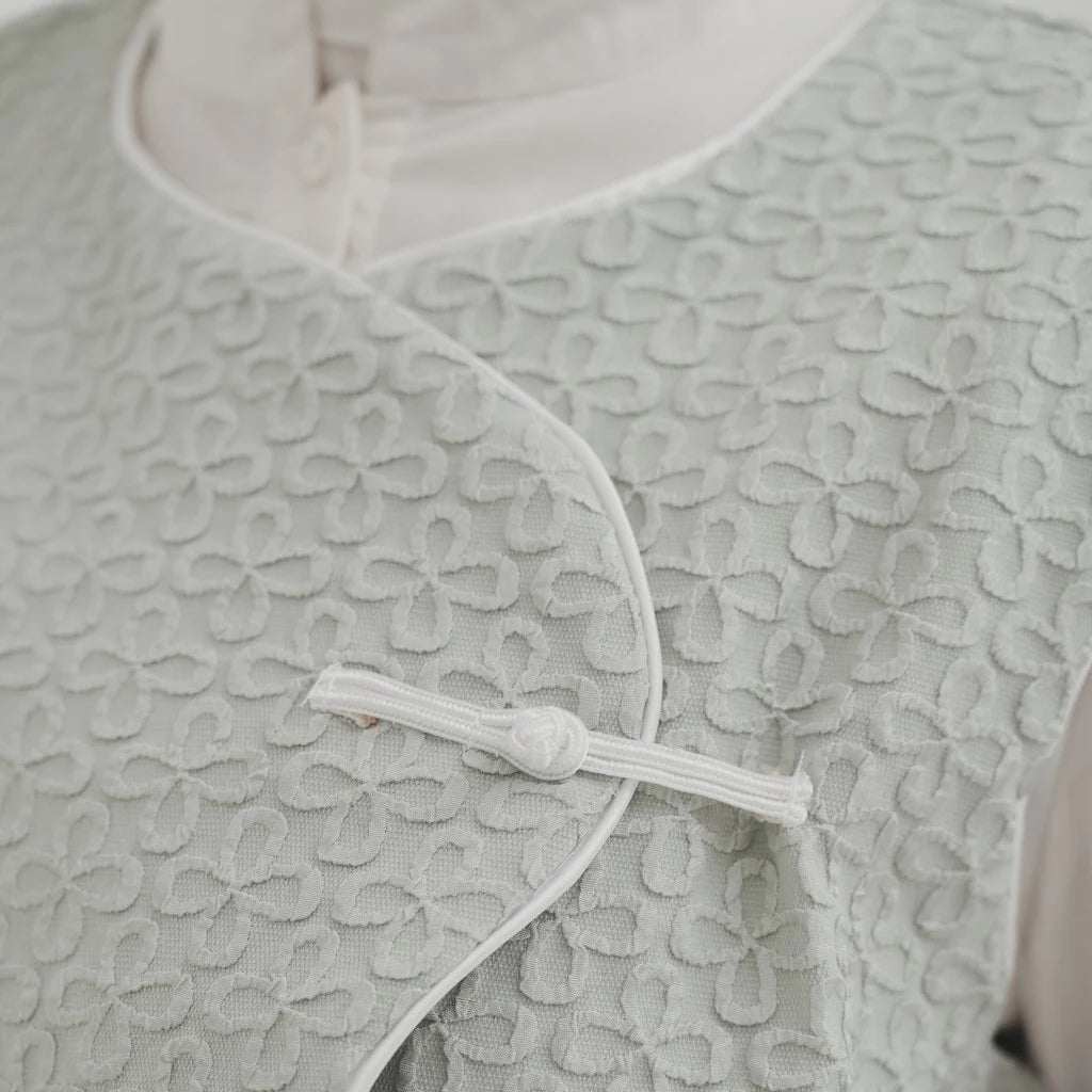 Close-up of a textured light gray vest with a button detail.