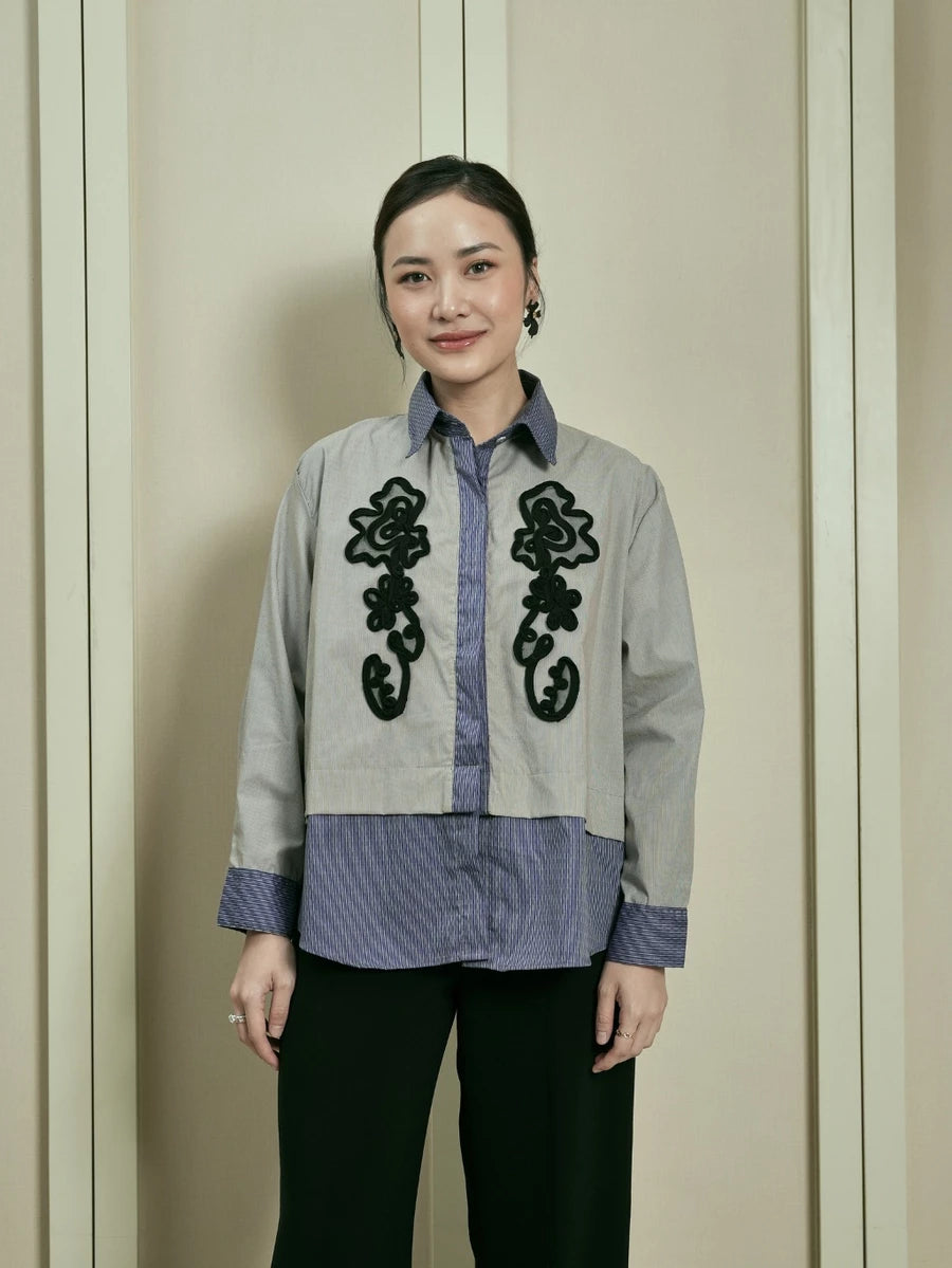 Woman wearing a light gray shirt by Studio Tui with black floral embroidery against a neutral background