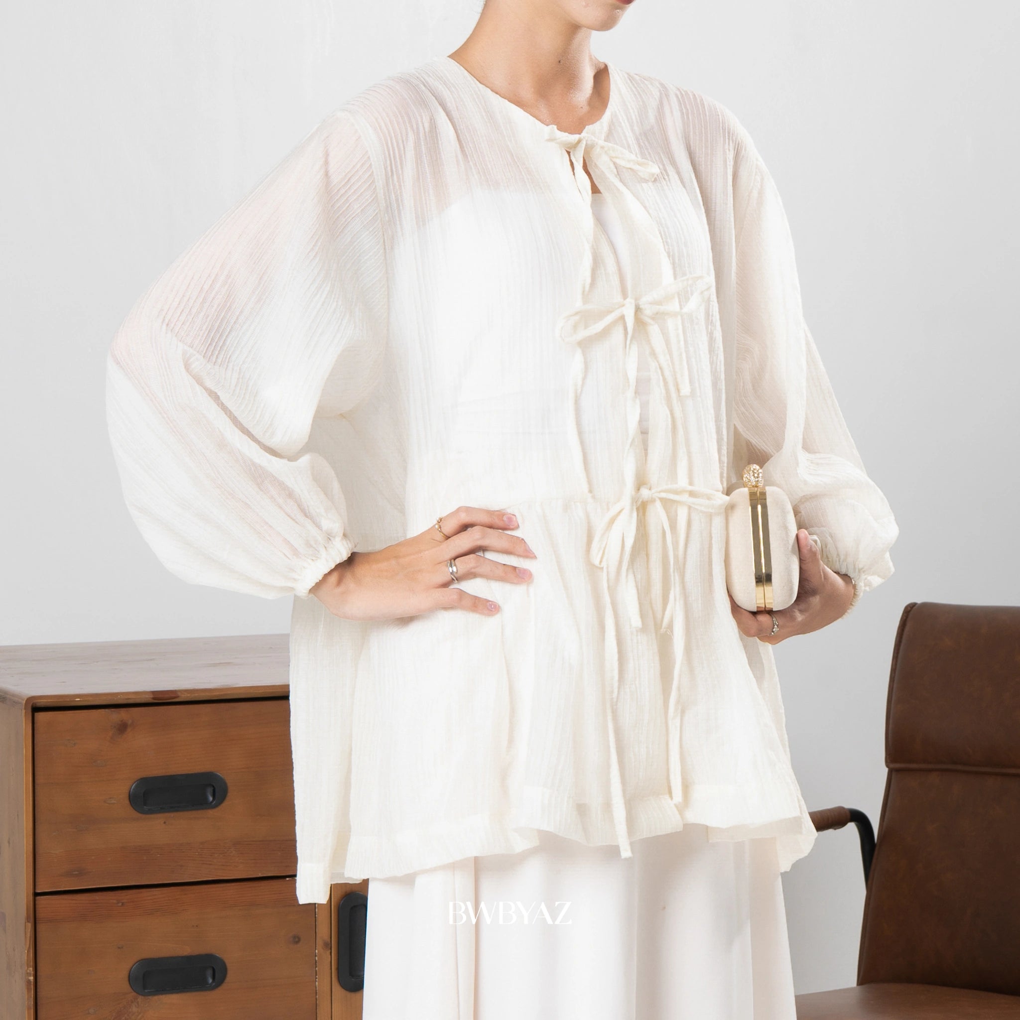 Person wearing a white outer by BWBYAZ holding a small clutch in a minimalistic setting.