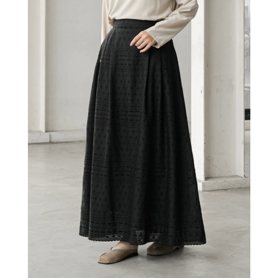 Person wearing a long black patterned skirt by Mistyvori with a white shirt in a minimalistic setting