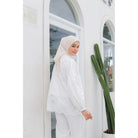 A person wearing a white balloon sleeve shirt with lace details by Casa Elana, paired with white trousers, standing next to a cactus plant.