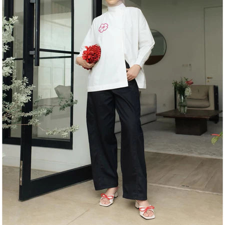 Person wearing a white shirt and black barrel pants from Haidee Orlin holding red flowers in a modern indoor setting.